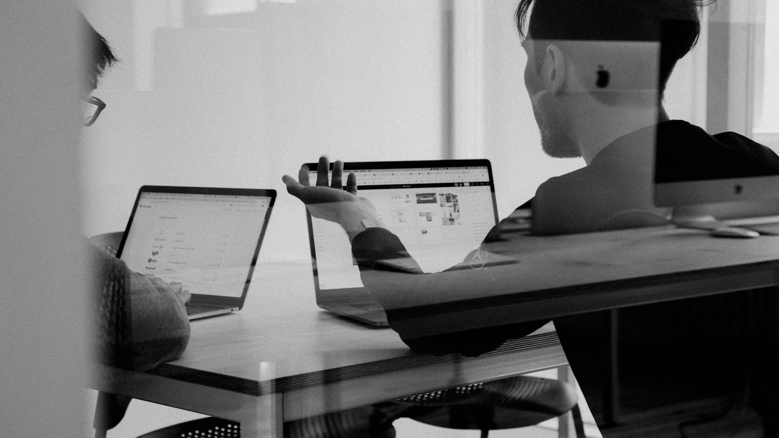 A founder at a desk reviewing a checklist of accounts and passwords next to a laptop showing a code repository